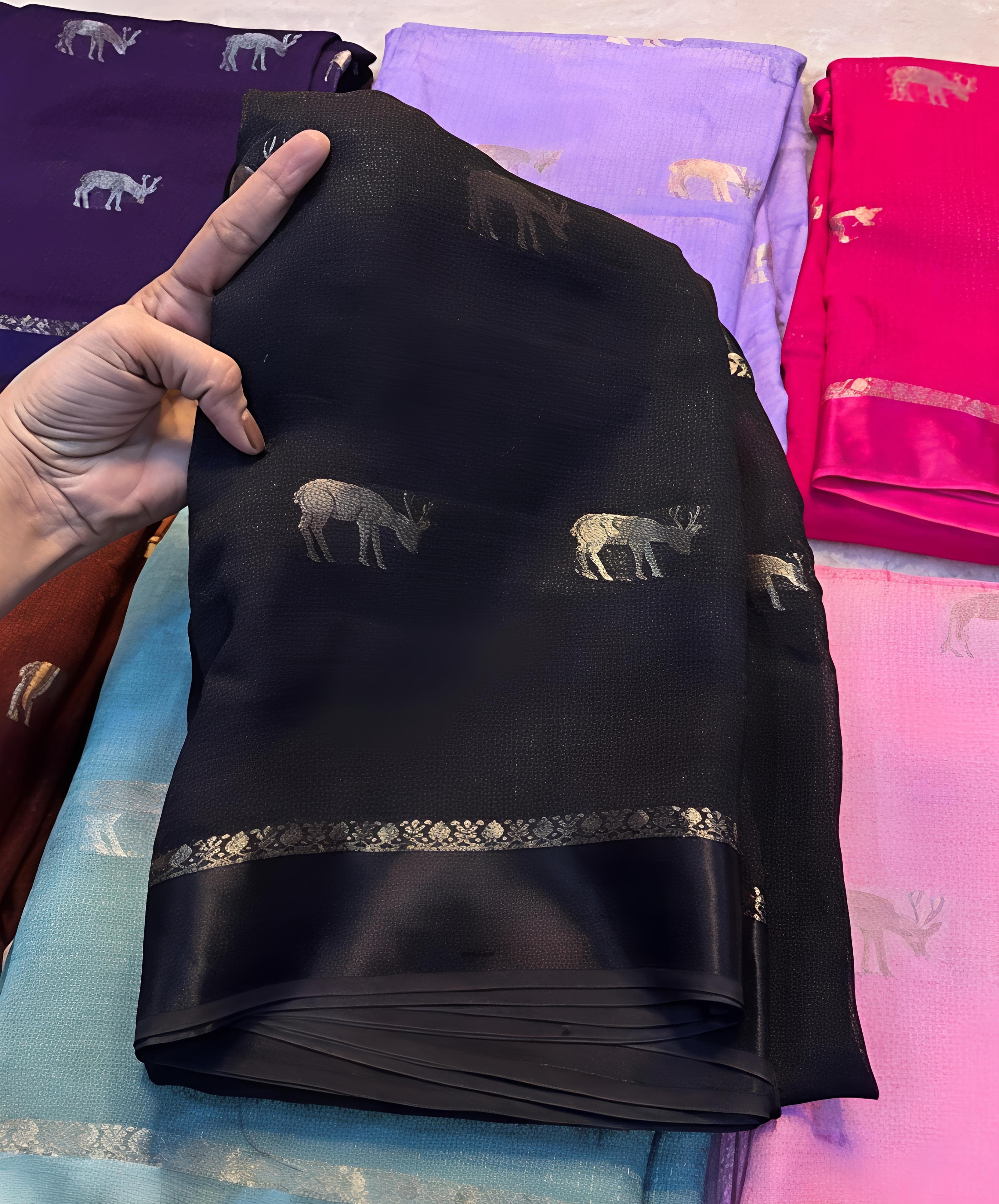 Black fabric with animal patterns held by a hand, with other colorful fabrics in the background.